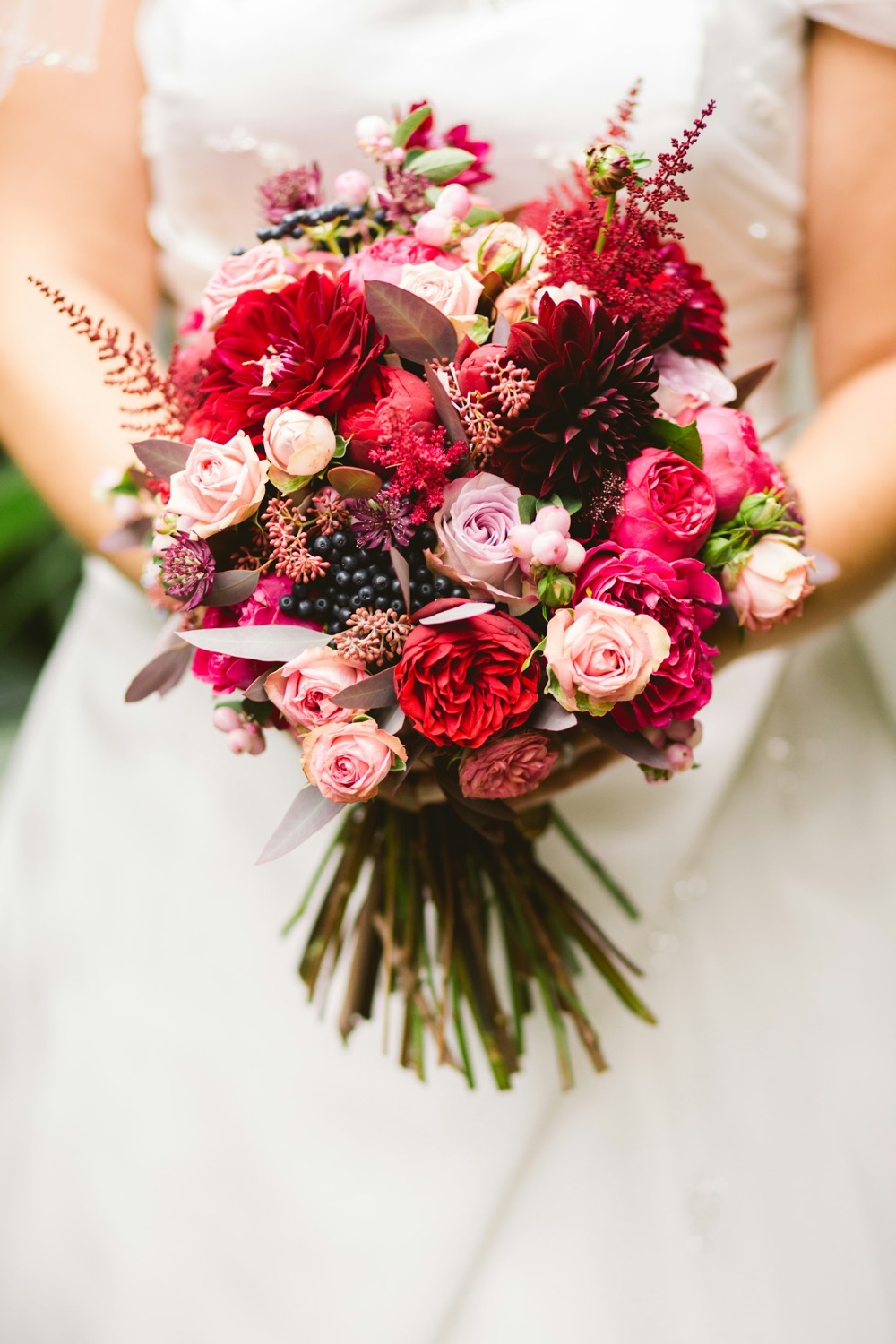 A bride holding a red and pink rose bouquet